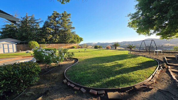 A backyard with a lawn, a swing set, and a view of distant hills.