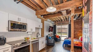 A modern kitchen with stainless steel appliances, a dining area with a brick wall, and a cozy seating space with a view. - Lowkey - Pool- Gym & Speakeasy - Mins to Broadway (Nashville)