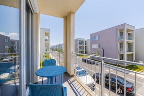 A balcony with two blue chairs and a table, overlooking a parking area and modern buildings. - Talea Holiday Apartments 2 Beach Pool Access (Shënkoll)