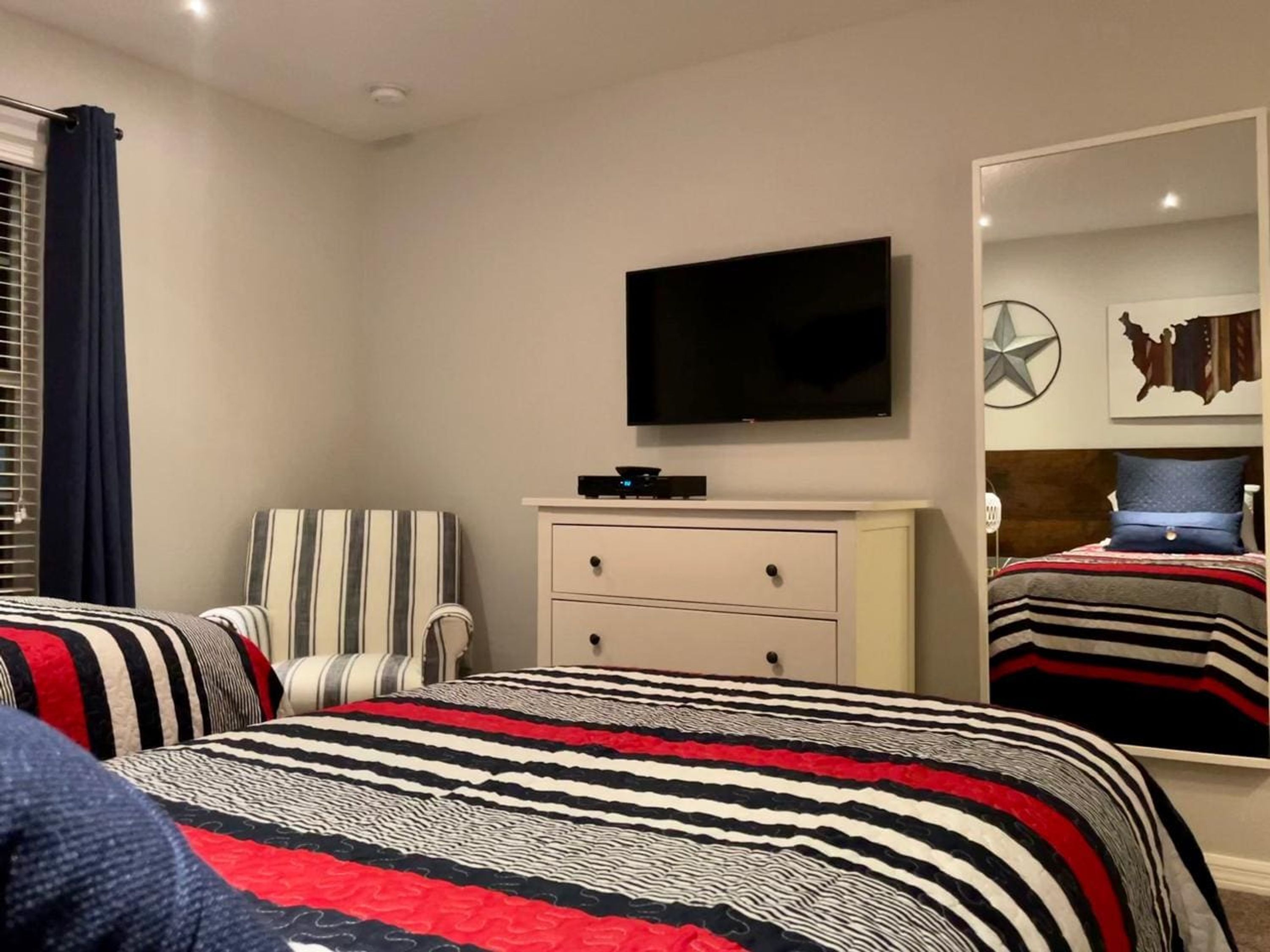 A bedroom with a bed, a chair, a dresser, a television, and a mirror.