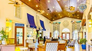 A spacious lobby with wooden ceiling beams, multiple ceiling fans, and a variety of seating arrangements including patterned chairs and sofas.