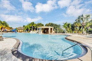 A swimming pool with a stone structure in the center, surrounded by palm trees and a clear sky.