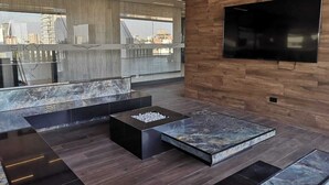 Un salon moderne doté d’un grand téléviseur, d’une cheminée et offrant une vue sur le paysage urbain grâce à de grandes fenêtres.