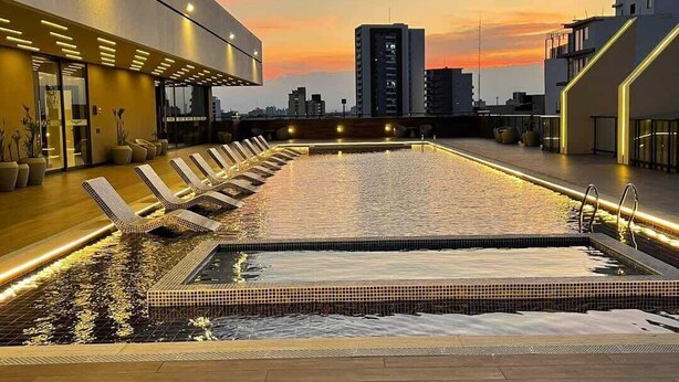 Une piscine sur le toit, dotée de chaises longues et offrant une vue sur la ville au coucher du soleil.