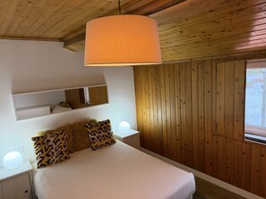 Un dormitorio con cama, lámpara colgante, mesita de noche con lámpara, espejo y paneles de madera en las paredes.
