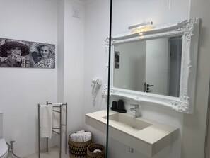Un baño con tocador blanco, un espejo grande con marco ornamentado, un perchero y un secador de pelo instalado en la pared.