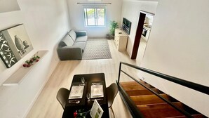 A modern living room with a sofa, dining table, and a staircase leading to another level. - AZORES PEDRA APARTMENTS - G (Fajã de Baixo)