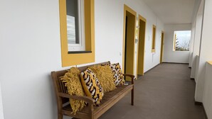 A corridor with a wooden bench, yellow-framed windows, and doors. - AZORES PEDRA APARTMENTS - G (Fajã de Baixo)