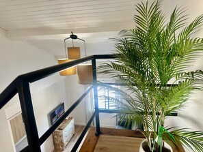 Una escalera con barandilla negra, una planta en maceta y una lámpara colgante.