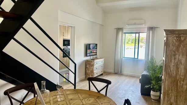 A modern living room with a dining table, chairs, a TV, and a staircase.