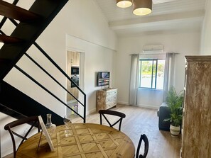 A modern living room with a dining table, chairs, a TV, and a staircase. - AZORES STONE APARTMENTS H (Fajã de Baixo)