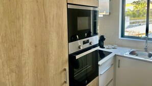 A modern kitchen with wooden cabinets, a built-in oven, a microwave, and a window with a view of greenery.