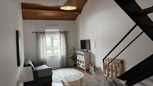 Un salon comprenant un canapé, une table basse en verre, un téléviseur, une bibliothèque et un escalier.
