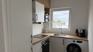 Une cuisine moderne avec des meubles blancs, un lave-vaisselle encastré, un lave-linge, une machine à café et une fenêtre laissant entrer la lumière naturelle.