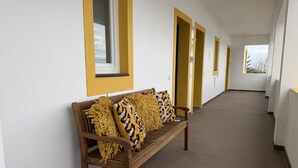 Un long couloir avec un banc en bois et des fenêtres à cadre jaune.