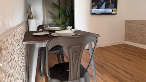 A dining area with a table set for four, a television mounted on the wall, and a potted plant. - AZORES PEDRA APARTMENTS A (Fajã de Baixo)