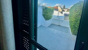 A view from a window overlooking a courtyard with a satellite dish, a small tree, and a building with a red roof. - AZORES PEDRA APARTMENTS A (Fajã de Baixo)