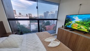 A bedroom with a large bed, a wooden dresser, a television, and a view of the city through a large window. - Inspiring views • Enveloping comfort (Santa Cruz de la Sierra)