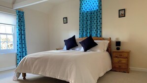 Een slaapkamer met een groot bed, twee kussens, een houten nachtkastje, een lamp en een raam met gordijnen.