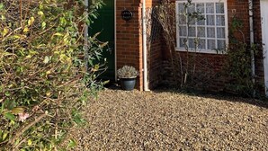 Een bakstenen huis met een pannendak, een groene deur en een kleine tuin met grind en planten.