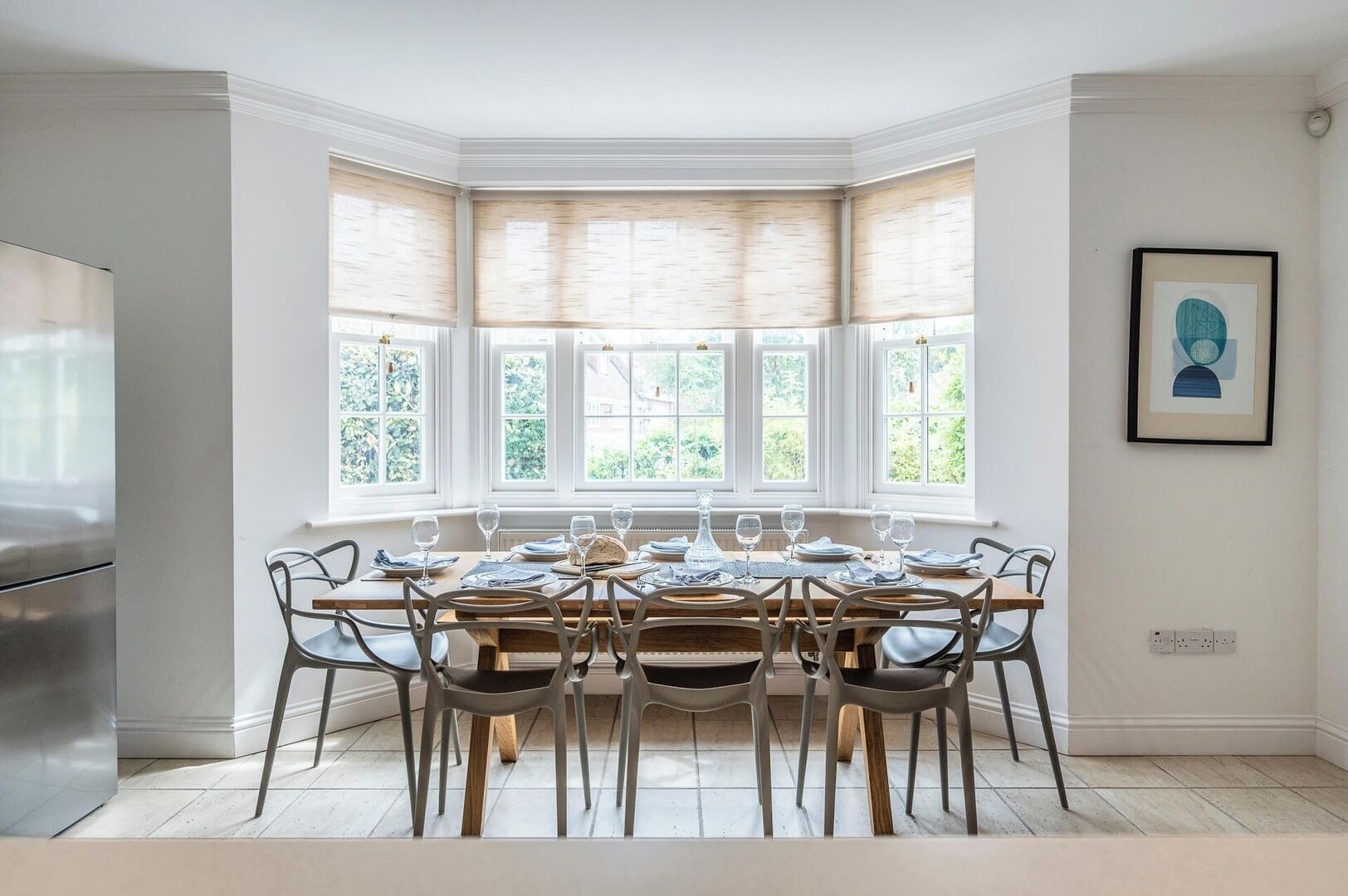 A dining area with a bay window, a stainless steel refrigerator, and a framed artwork on the wall.