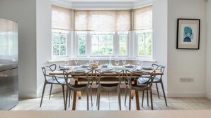 A dining area with a bay window, a stainless steel refrigerator, and a framed artwork on the wall.
