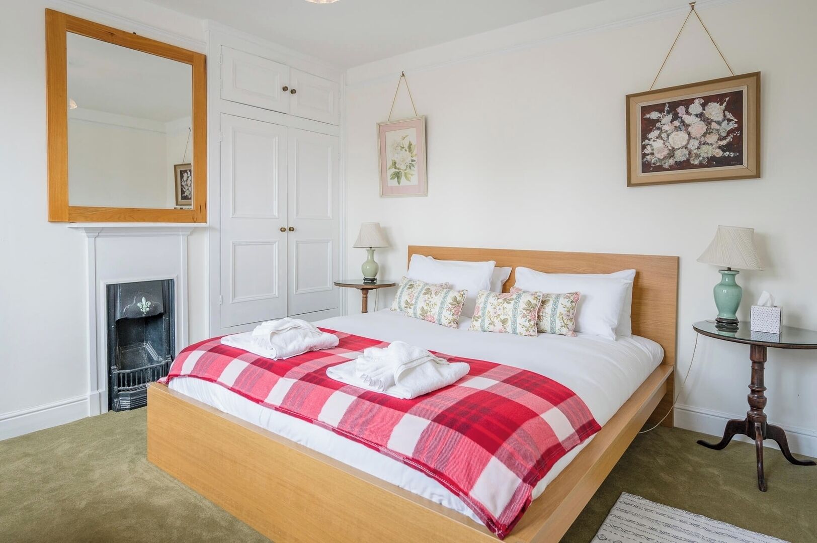 A neatly arranged bedroom with a bed, a fireplace, and two wall-mounted lamps.