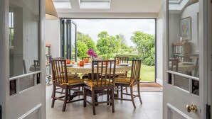 A dining area with a round table, chairs, and a view of a garden through large windows.