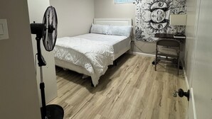 A bedroom with a bed, a standing fan, a window, and a wall with a black and white pattern. - Looking for a clean place to rest that won’t break the bank? Nestle offers that. (Woodbridge Township)