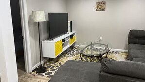 A living room with a sofa, a glass coffee table, a TV on a white cabinet, and a patterned rug. - Looking for a clean place to rest that won’t break the bank? Nestle offers that. (Woodbridge Township)