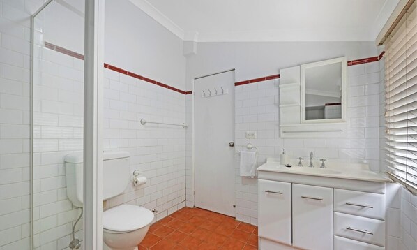 A bathroom with white tiles, a toilet, a sink with a mirror, and a shower area.