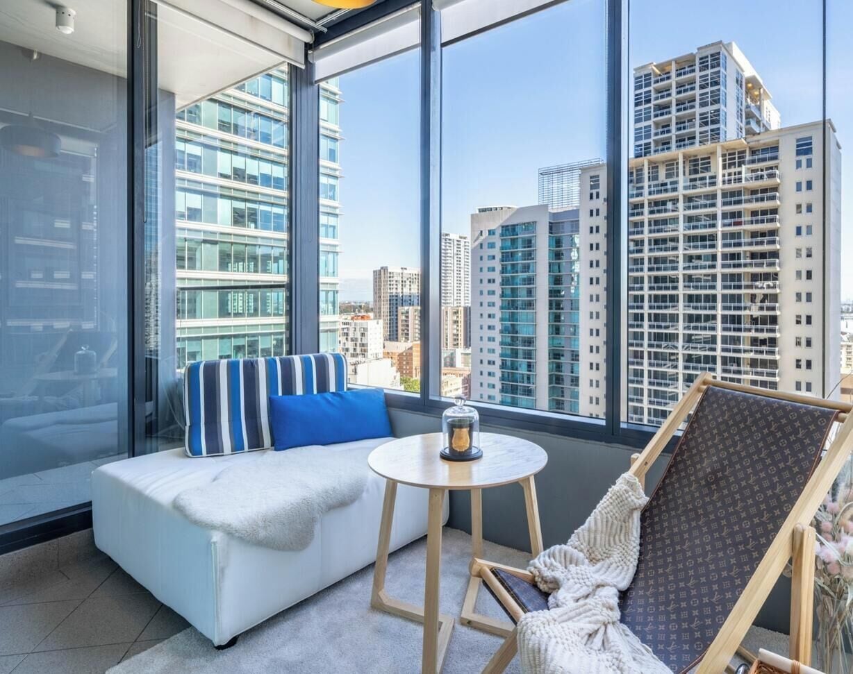 A modern room with a sofa, a small table, and a chair, large windows with a city view.