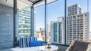 Une chambre moderne avec un canapé, une petite table et une chaise, de grandes fenêtres offrant une vue sur la ville.