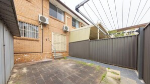A brick building with a gated backyard, a metal fence, and a covered patio area. - KozyGuru | Cabramatta | Spacious 3BR Townhouse (Cabramatta)