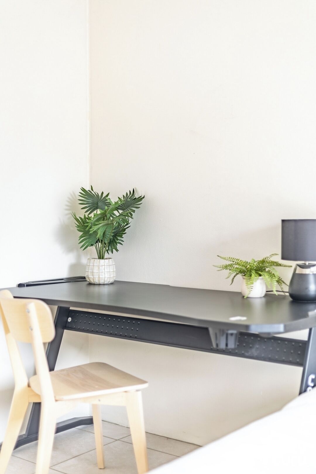 A modern desk with a chair, a potted plant, and a small table with another plant.