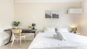 A hotel room with a bed, a desk with a chair, a lamp, and two wall-mounted air conditioners. - KozyGuru | Cabramatta | Spacious 3BR Townhouse (Cabramatta)