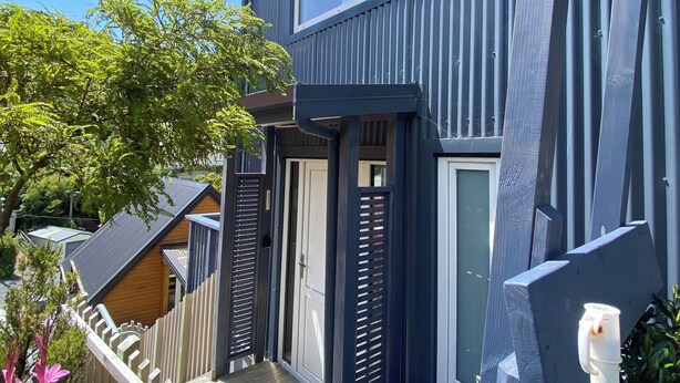 A modern two-story building with a balcony, a wooden fence, and a clear blue sky. - 3 Bedroom Passive Haus in the lush Aro Valley (Wellington)