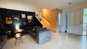 A modern living room with a dark blue accent wall, a grey sofa, a wooden staircase, and a large white door. - 3 Bedroom Passive Haus in the lush Aro Valley (Wellington)