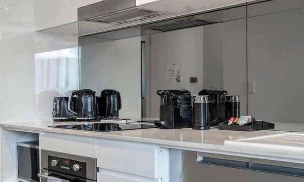 A modern kitchen with a stainless steel range hood, a built-in oven, and a coffee station with multiple coffee makers. - KozyGuru | CBD Darling Harbor | View Stunning Loft (Sydney)