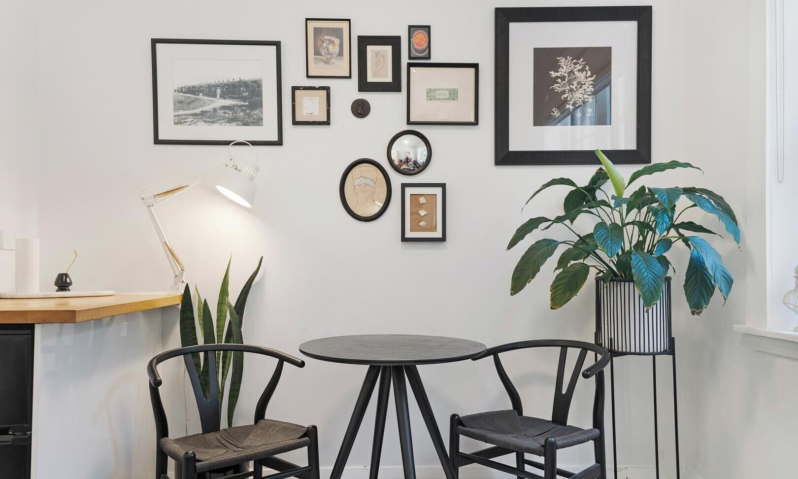A room with a round table, two chairs, a potted plant, and various framed pictures on the wall.