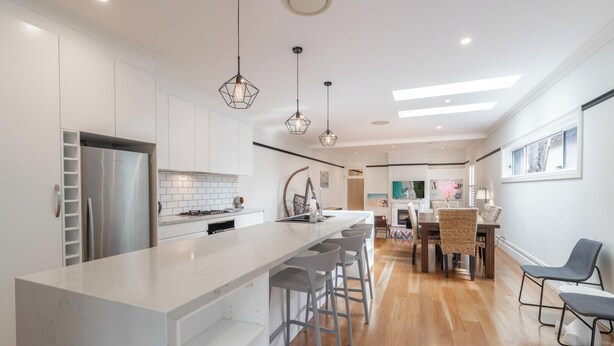 Una cocina moderna con una isla central, taburetes de bar e iluminación colgante.
