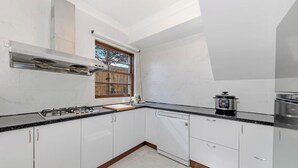 A kitchen with white cabinets, a gas stove, a dishwasher, and a window with a view of the outdoors. - KozyGuru | Thornleigh | Charming Two-Bed Townhouse (Thornleigh)