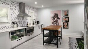 A modern kitchen with a central island, white cabinetry, and a black metal frame table. - Insta-Worthy Modern House in the Heart of Miami (Miami)