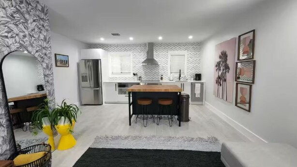 A modern kitchen with a central island, a refrigerator, and a dining area with chairs. - Insta-Worthy Modern House in the Heart of Miami (Miami)