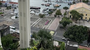 Uma marina com vários barcos atracados, uma torre branca imponente e um edifício com a placa 'Mercado Modelo'.