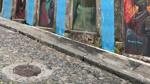Um edifício com murais coloridos nas portas e janelas, uma rua de calçada e uma tampa de bueiro.