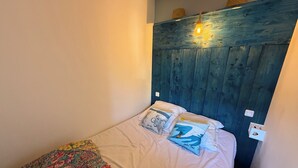 Een kleine, knusse slaapkamer met een eenpersoonsbed, een deken met bloemenprint en een blauw hoofdbord.