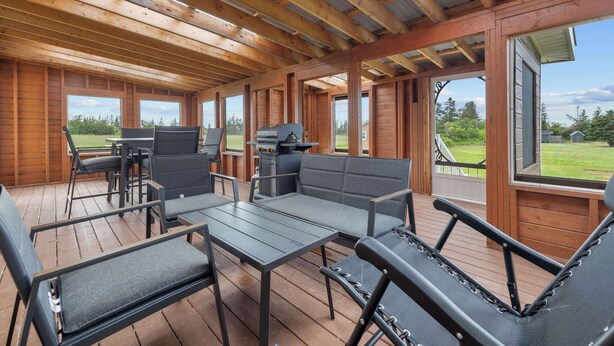 A covered outdoor seating area with wooden beams, a grill, and a view of the outdoors. - Charming 2-Bed Cottage in Savage Harbour with Beach & Enclosed Sunroom (Prince Edward Island)