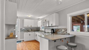 A modern kitchen with white cabinetry, a central island with stools, a microwave, and a stove. - Charming 2-Bed Cottage in Savage Harbour with Beach & Enclosed Sunroom (Prince Edward Island)