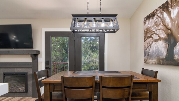 Un comedor con una gran mesa de madera, cuatro sillas, una chimenea, un televisor y un cuadro grande de un árbol en la pared.